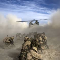 Ground troops stay low to the ground while a Chinook helicopter lands.